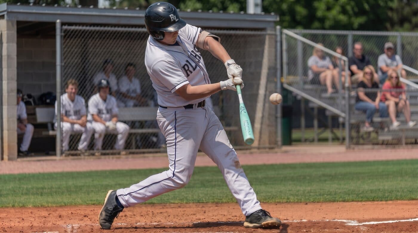 High school batter making contact with the pitch at home plate, ball just off the bat